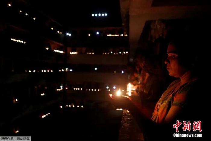 资料图：当地时间4月5日21点，印度民众熄灯9分钟，点燃蜡烛和油灯为抗疫祈福。图为孟买民众在阳台上捧起烛光。