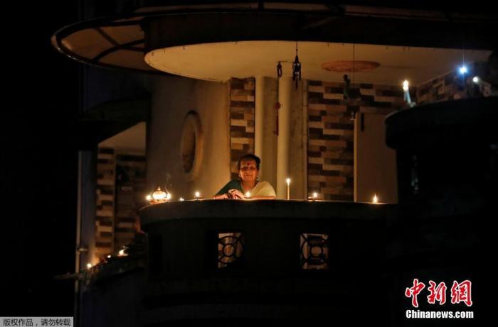 当地时间4月5日21点，印度民众熄灯9分钟，点燃蜡烛和油灯为抗疫祈福。图为印度艾哈迈达巴德一名妇女点燃蜡烛站在阳台上。