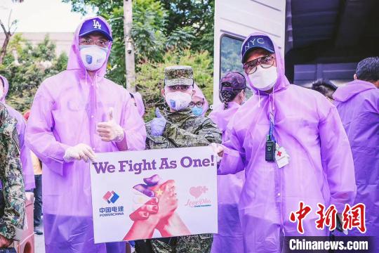 　捐赠现场，以紫色雨衣作为防护衣的志愿者，将一袋袋大米捐赠给菲律宾基层社区。宣传版上是紧握的两只手，绘以中菲两国国旗，口号是“WE FIGHT AS ONE!” 爱+慈善基金会供图 摄