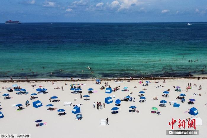 资料图：当地时间6月10日，美国佛罗里达州迈阿密海滩关闭近三个月后首次开放，工作人员在场提醒游客保持社交距离的前提下享受阳光沙滩。