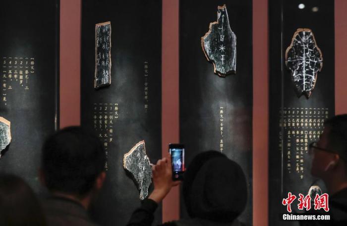资料图：10月22日，“证古泽今——甲骨文文化展”在北京中国国家博物馆开幕。展览通过近190件甲骨、青铜、玉石、书籍实物构成的叙事链条，讲述甲骨发现与发掘的惊世过往，重温甲骨文背后的商周文明，致敬相关学者们的卓越成就。这是国家博物馆第一次举办以甲骨文为内容的文化展，也是国家博物馆馆藏甲骨的第一次大规模展示。图为甲骨碎片放大模型及译文注释吸引观众。<a target='_blank'  data-cke-saved-href='http://www.chinanews.com/' href='http://www.chinanews.com/'>中新社</a>记者 贾天勇 摄