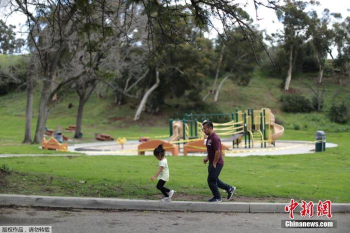 资料图：当地时间3月23日，在美国加利福尼亚州洛杉矶，一对父母走过一个封闭的游乐场。