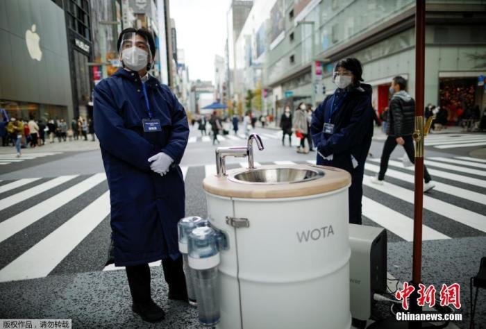 当地时间12月19日，日本东京银座购物区，工作人员站在一台名为“WOSH”的移动式洗手机旁。这台机器可以为路人提供方便的洗手清洁服务，有助防范新冠病毒。