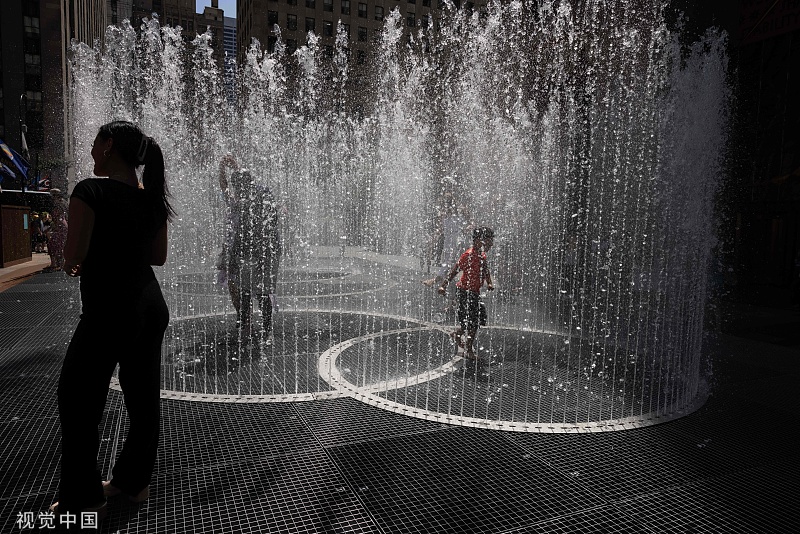 当地时间2022年7月19日，美国纽约，热浪席卷欧洲和北美，人们在纽约洛克菲勒中心广场畅玩艺术家杰佩·海因的水基雕塑《变化的空间》。人民视觉 图