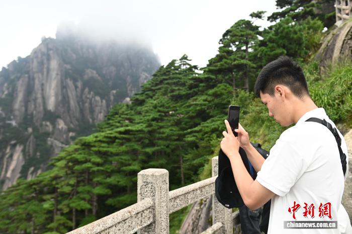 中国侨网8月12日，“徽风探源——2025华裔大学生中国文化体验营”走进安徽黄山风景区，学生们通过脚步丈量自然之美，沉浸式感受黄山生态与人文交织的独特魅力。图为华裔学生用手机记录黄山景色。中新社记者 韩苏原 摄　